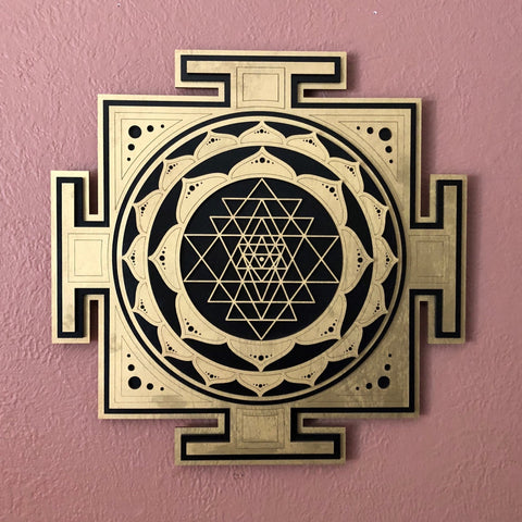 Gold and black Divine Sri Yantra against a mauve wall